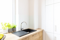 Black sink in wooden countertop in white kitchen interior with window. Real photo