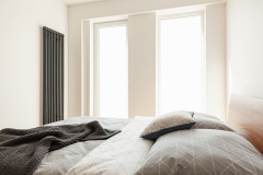 Blanket and grey pillows on bed in simple white bedroom interior with windows. Real photo