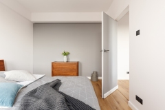 Grey bedroom interior with a blanket on a bed, chest of drawers with a plant, boxes on the floor and opened door