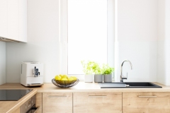 Wooden cabinets in bright minimal white kitchen interior with window. Real photo